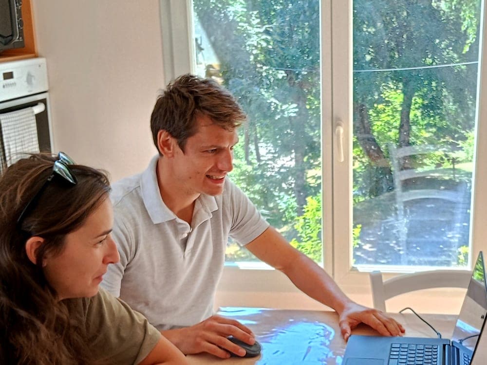 Simon explique un outil d’IA à une cliente, chez elle, devant un ordinateur portable